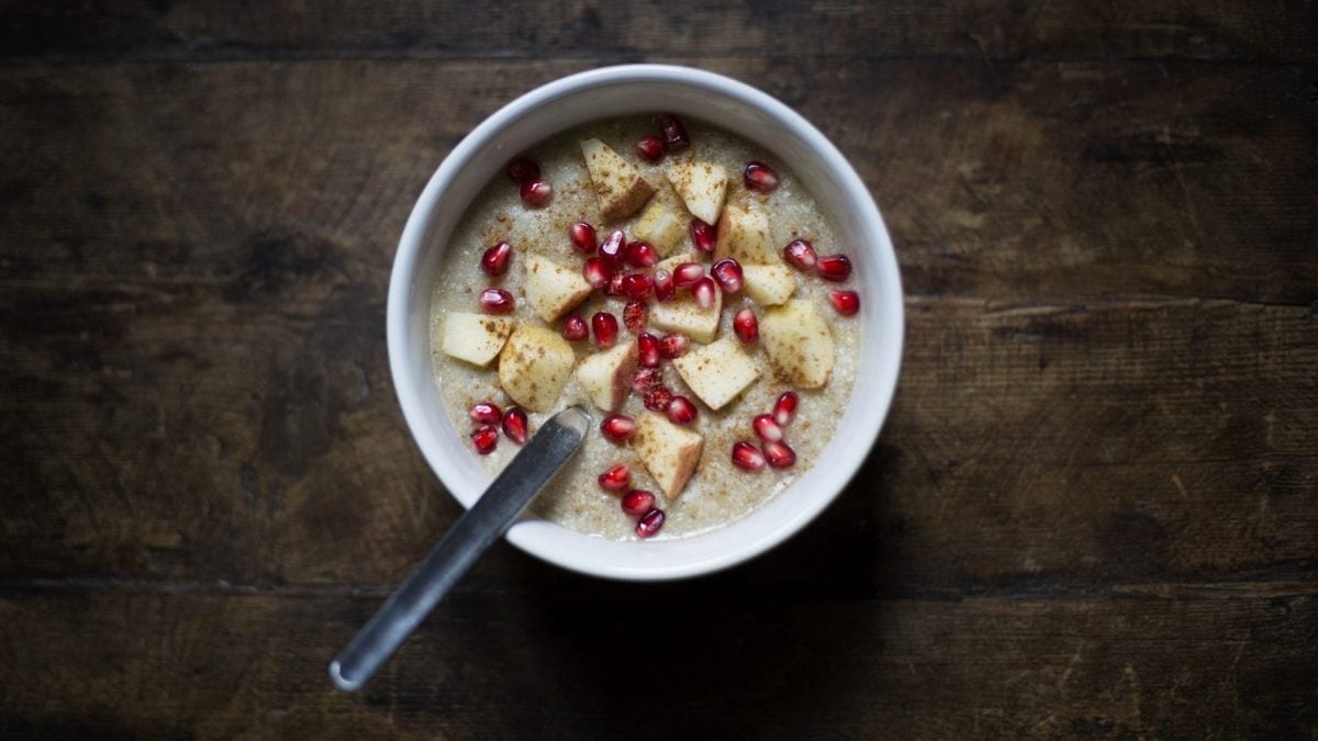 Aus der Vogelperspektive: Auf einem dunklen Holztische steht eine Schüssel mit Apfel-Zimt-Porridge. In der Schüssel ist ein Löffel.