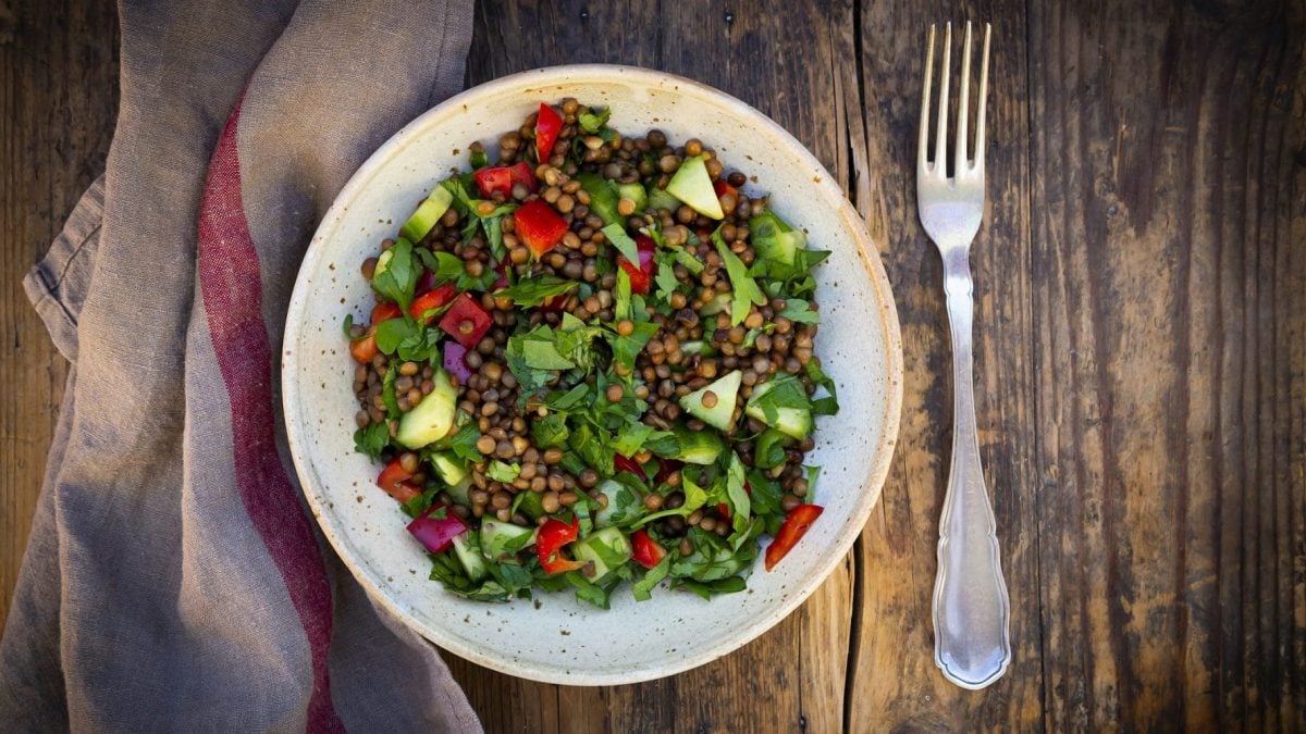 Aus der Vogelperspekttive: Auf einem Tisch steht ein teller mit einem warmen Balsamico-Linsen-Salat. Daneben liegt eine Gabel.