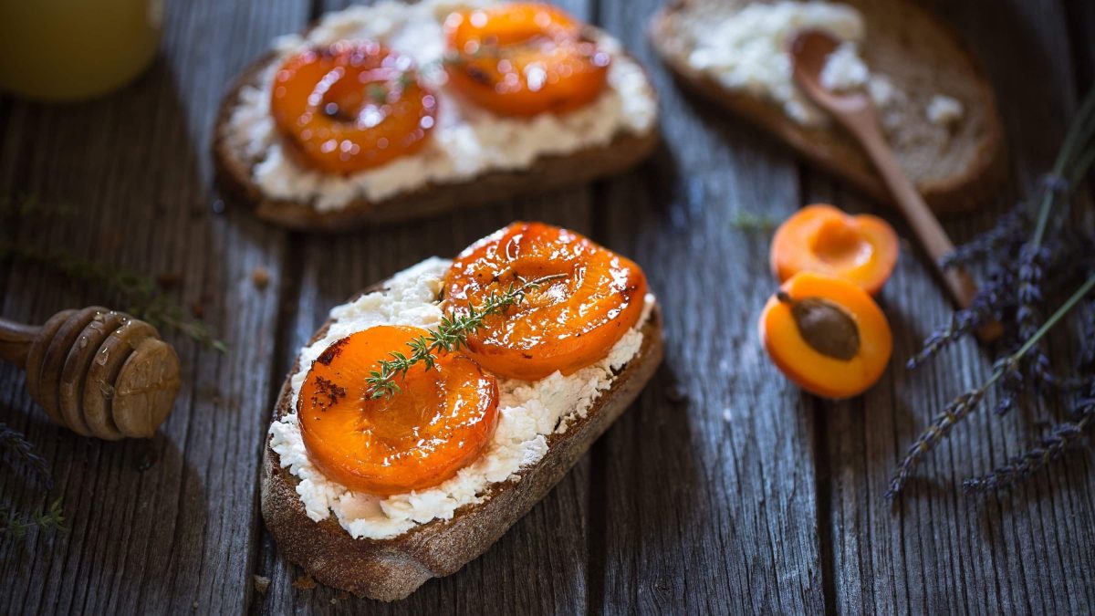 Knursprige Crostinis mit Ziegenkäse und Aprikose, garniert mit Thymian und Honig auf einer Holzplatte mit frischen Lavendelblättern im Hintergrund