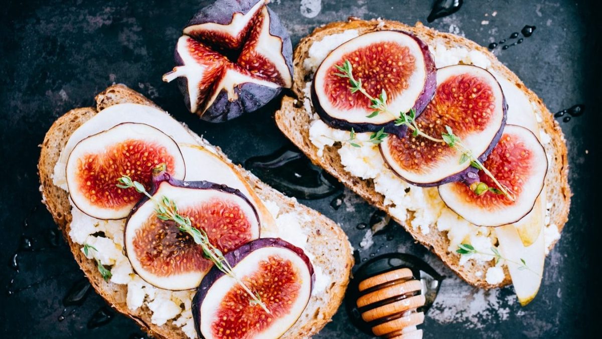 Zwei Scheiben Feigen-Ziegenkäse-Brot liegen auf einer schwarzen Schiefertafel.
