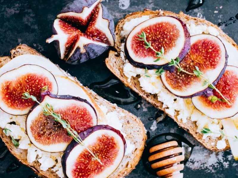 Zwei Scheiben Feigen-Ziegenkäse-Brot liegen auf einer schwarzen Schiefertafel.