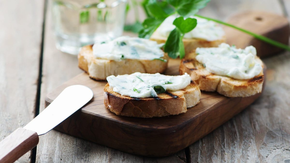 Getoastete Brotscheiben mit selbst gemachtem Frischkäse auf einem Brett, daneben liegt ein Messer.