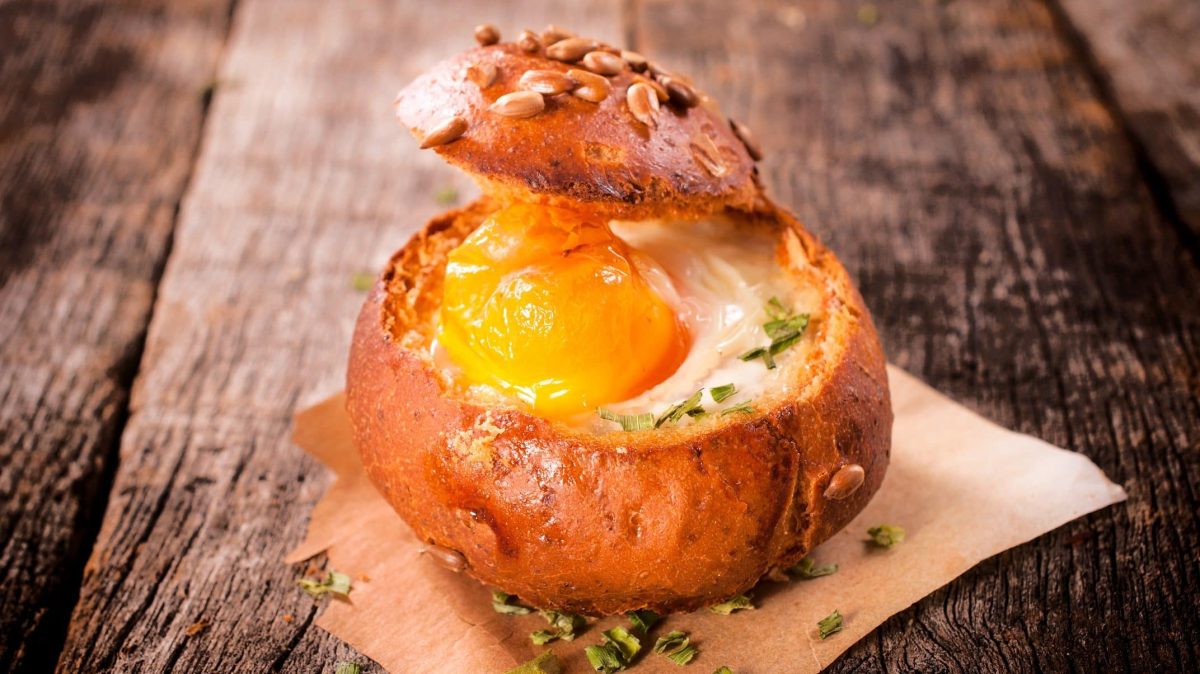 Unsere Frühstücks-Bowl im Brötchen steht auf Backpapier auf einem Holztisch.