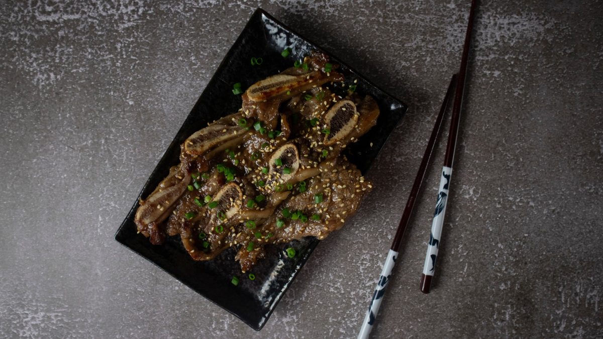 aufnahme von galbi von oben auf eckigem teller mit stäbhcen auf grauem tisch
