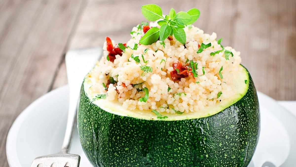 Auf einem Tisch steht ein teller. Auf dem Teller steht eine gefüllte Zucchini mit Couscous. Auf dem Teller liegt auch noch eine Gabel.
