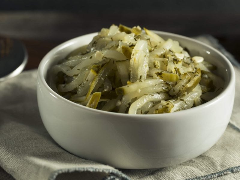 Eine Schale Dill-Gurken-Relish auf einem Geschirrtuch, daneben ein Löffel.