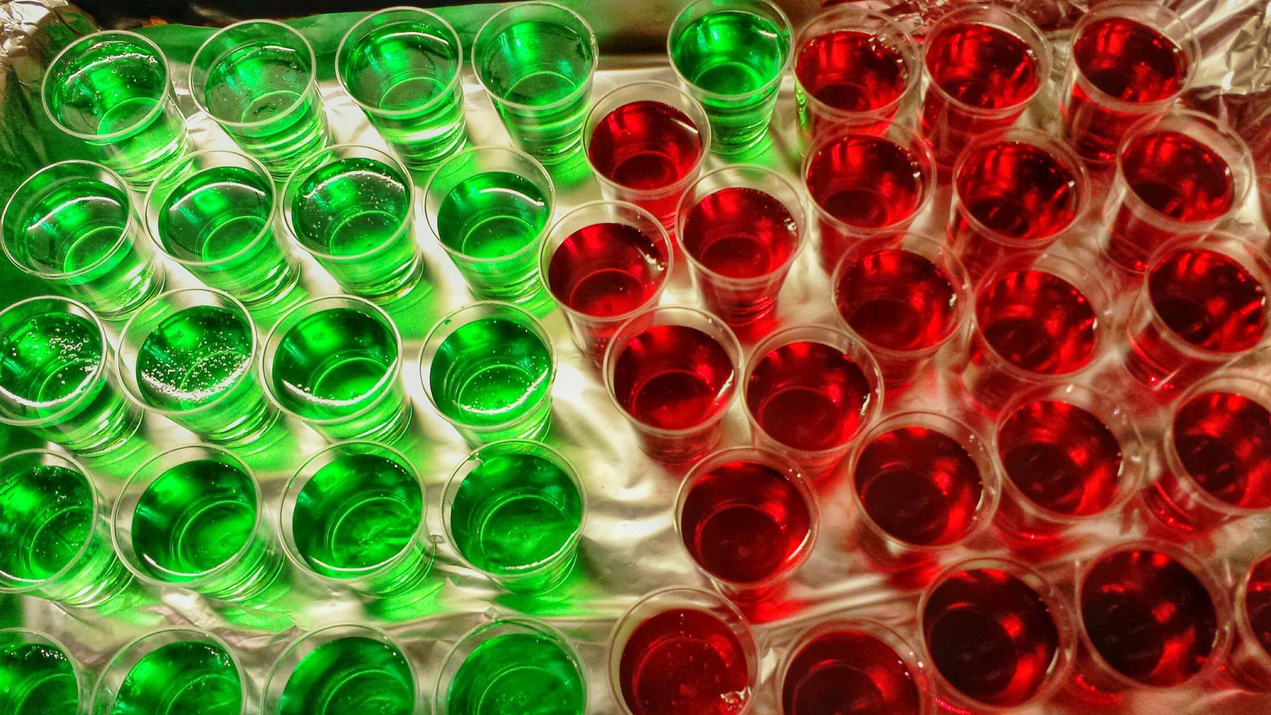 Grüne und rote Jell-o Shots Jelly Shots in kleinen Gläsern auf hellem UNtergrund. Aufnahme aus der Vogelperspektive.