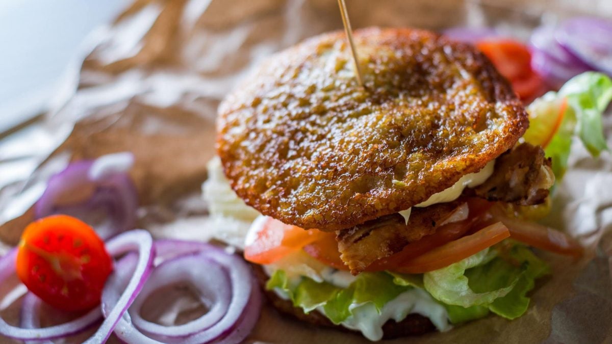 Kartoffel-Burger mit Burgerpatty, Salat und Tomaten, daneben liegen einige Zutaten.