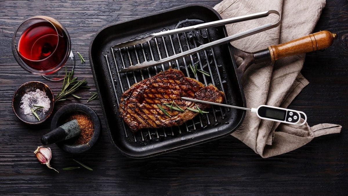 Ein Rinderfilet liegt in einer Grillpfanne, die auf dem Tisch steht. Im Rinderfilet steckt ein Thermometer.