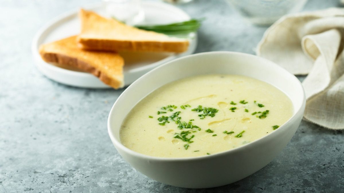 In einer weißen Schüssel ist eine meerrettich-kartoffel-suppe. Neben der Schüssel liegen zwei Toast-Hälften