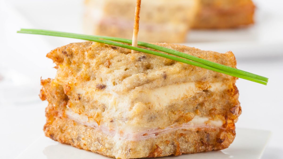 Monte Christ Sandwich auf weißem Teller vor weißen Hintergrund. Oben auf ein Schnittlauchzweig. Frontalansicht.