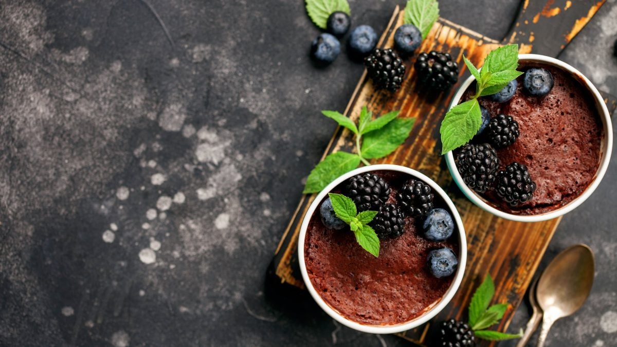 Zwei Schokodesserts von oben, auf Holzbrett und schwarzem tisch mit Beeren und Minze.