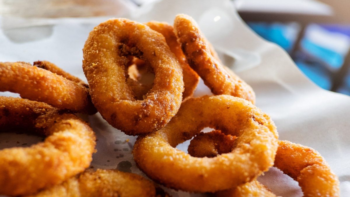 Ein paar Onion Rings in Bierteig auf einer weißen Servierplatte.