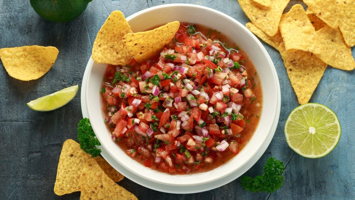 Eine Schüssel Salsa mit Nachos in der Draufsicht, daneben liegen weitere Chips und Limetten.
