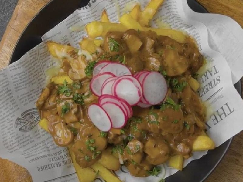 Unsere Poutine, angerichtet auf Zeitungspapier in einem schwarzen Teller.