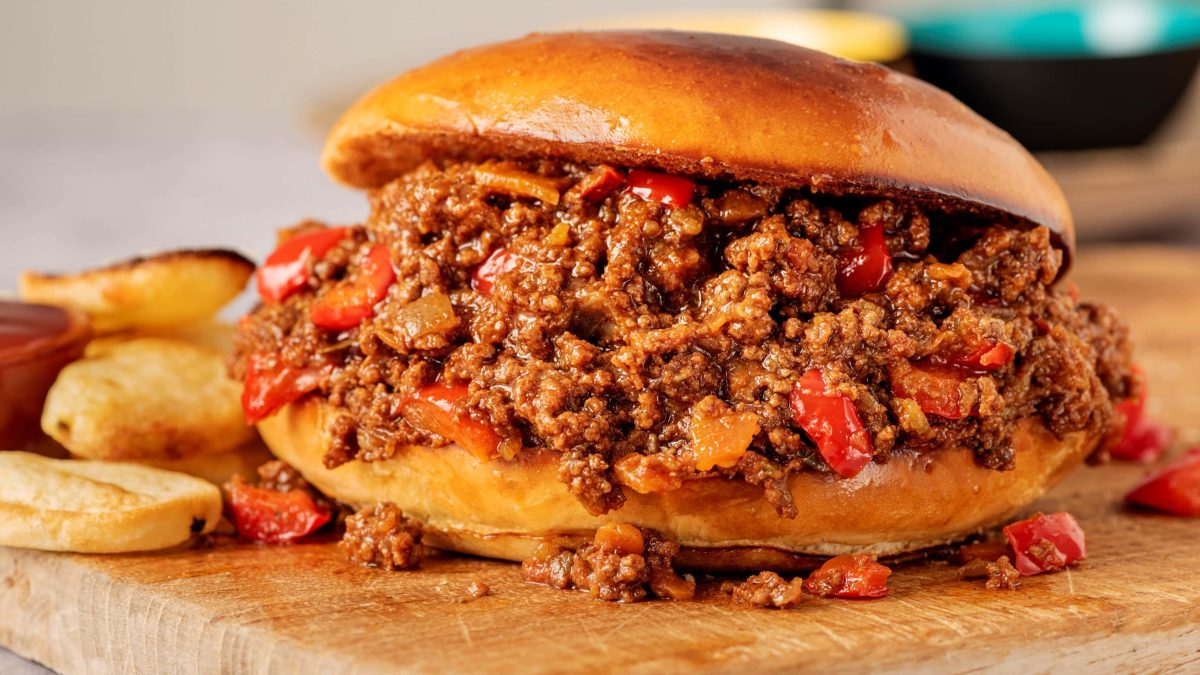 Seitliche aufnahme eiens sloppy joes mit Kartoffeln im hintergrund auf holzbrett