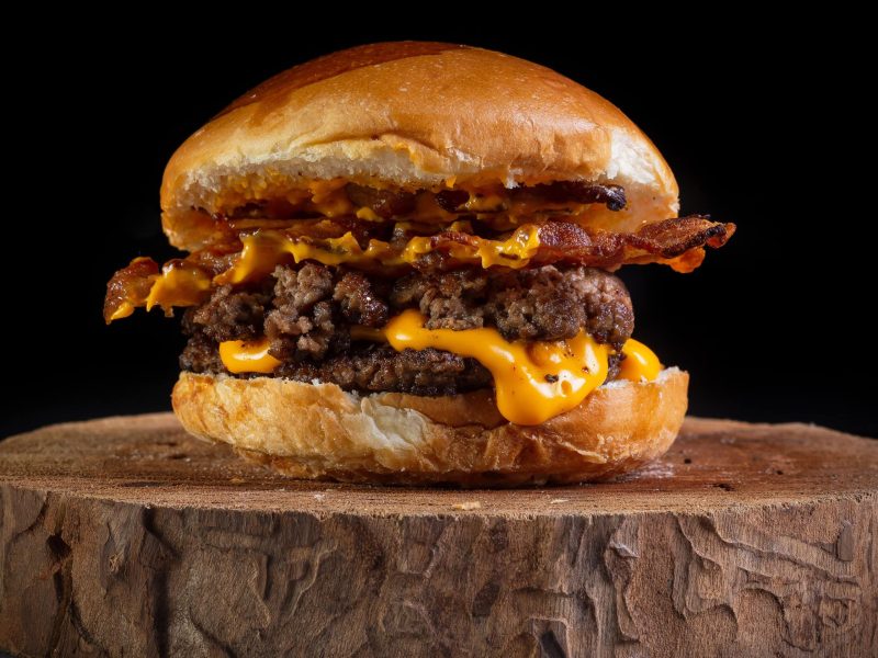 Unser Smashed Bacon-Cheeseburger liegt auf einem Holzbrett.