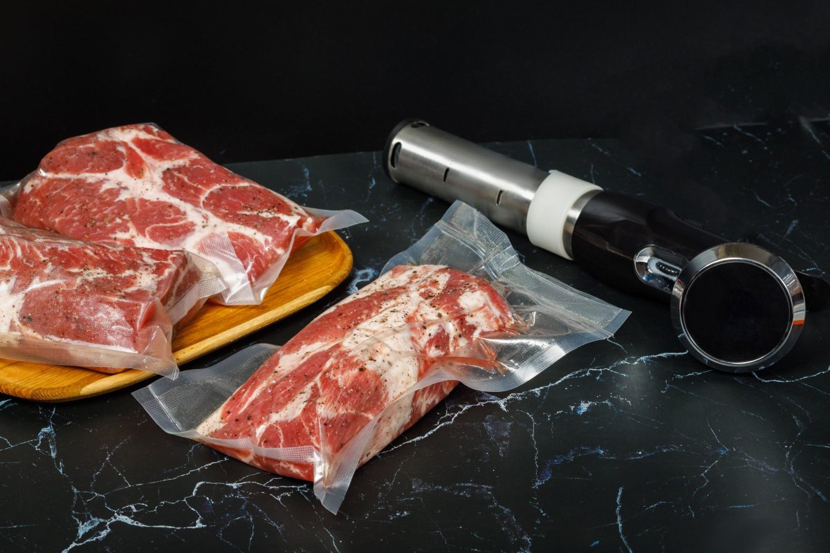Sous-Vide Stab rechts und zwei vakuumierte Beutel mit rindfleisch links auf schwarzem Tisch