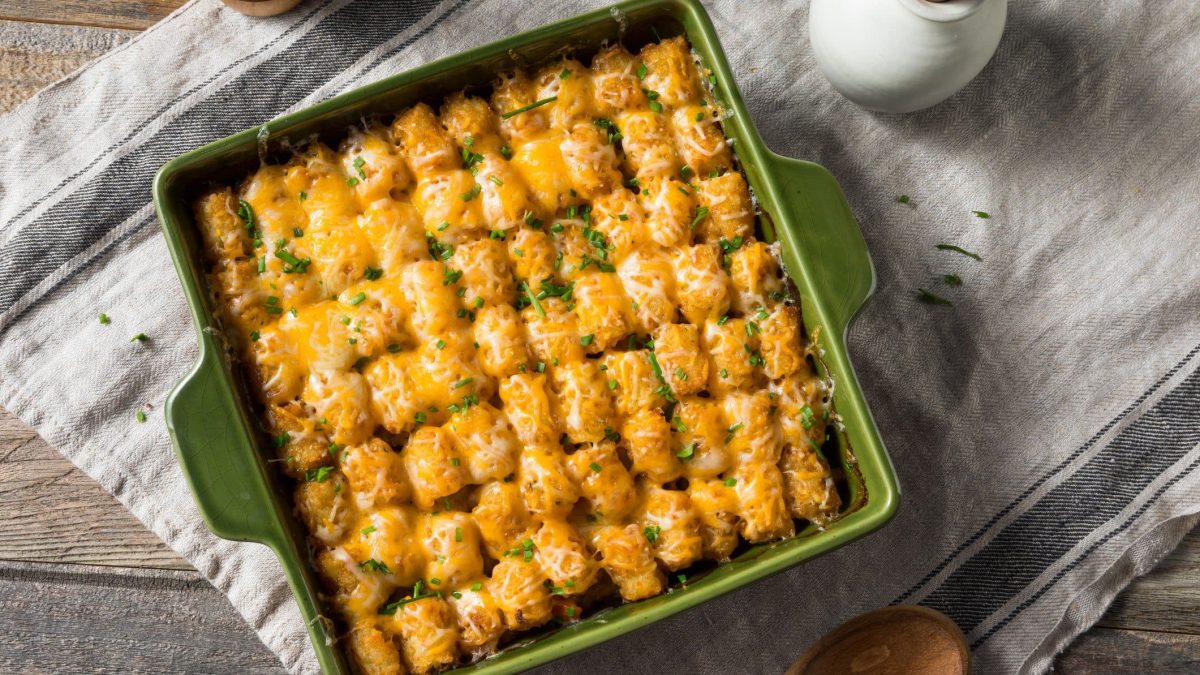 Tater Tot Hot Dish in grünr Auflaufform auf Tuch und Holztisch. Aufnahme aus der Vogelperspektive.