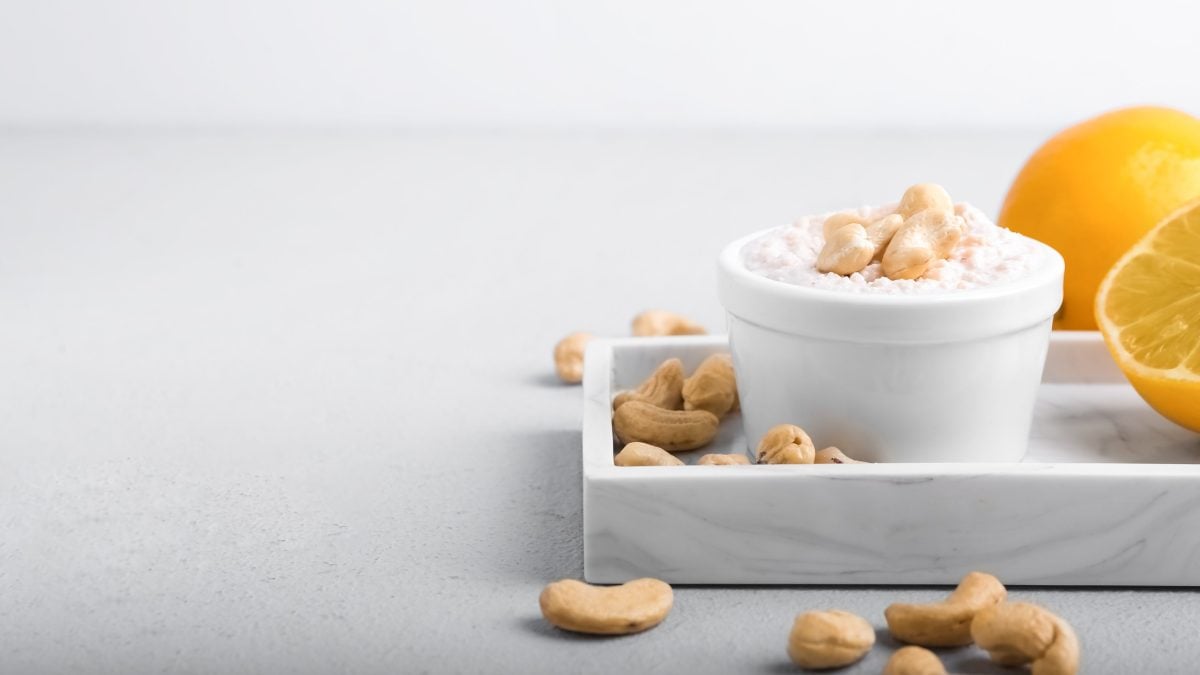Eine Schale vegane Sour Cream mit Cashekernen auf einem Tablett, daneben liegt eine halbierte Zitrone.