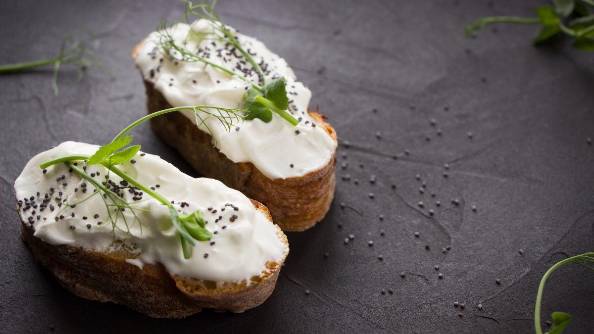 Veganer Frischkäse auf Brotscheiben, garniert mit Microgreens auf einer schwarzen Schieferplatte