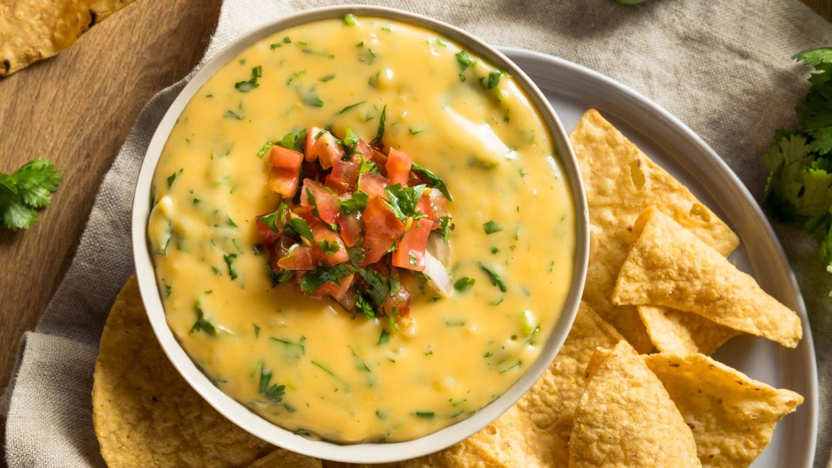 Eine Schale veganer Käsedip mit geschnittenen Tomaten und Kräutern sowie Nachos.