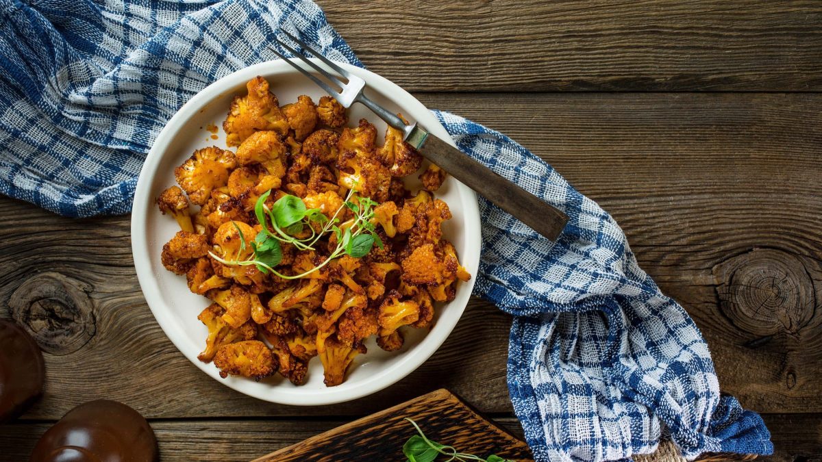 Ein knuspriges veganes Blumenkohl-Gyros aus dem Ofen auf einem großen weißen Teller mit Kräutern garniert