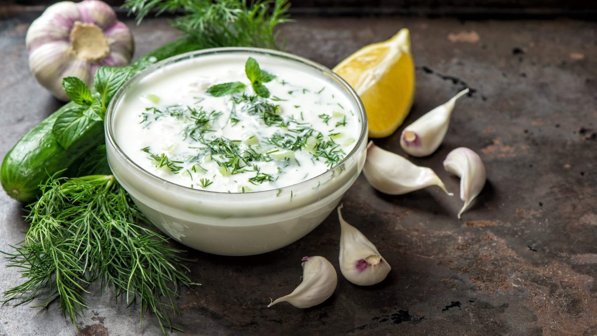 Eine große Schale mit veganem Tzaziki mit Zitrone, Kräutern, frischem Knoblauch und saftiger Gurke auf einem steinernen Tisch