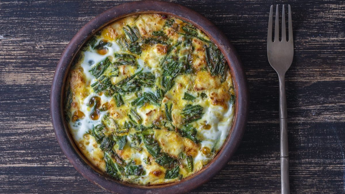 Aus der Vogelperspektive: Auf einer dunklen Holzplatte steht eine Keramkschüssel, in der eine Vegetarische Bärlauch-Frittata ist.