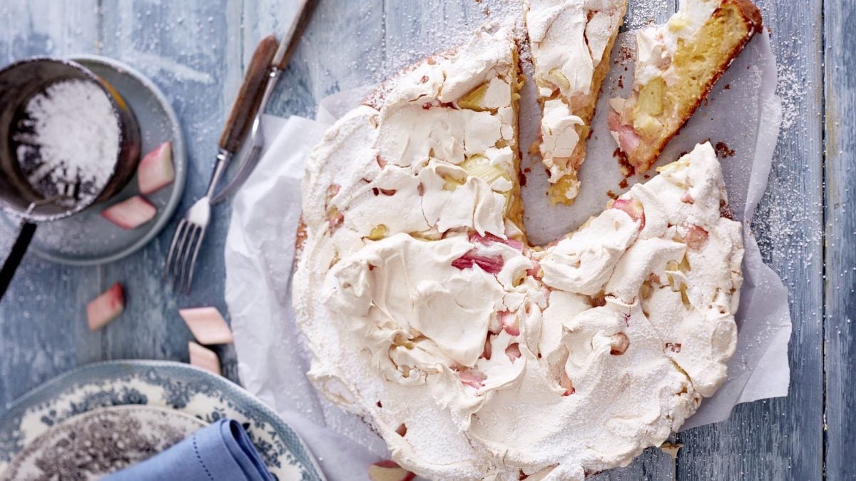 Auf einem Teller liegt ein Rhabarber-Orangen-Kuchen. Er ist bestrichen mit cremigem Baiser.