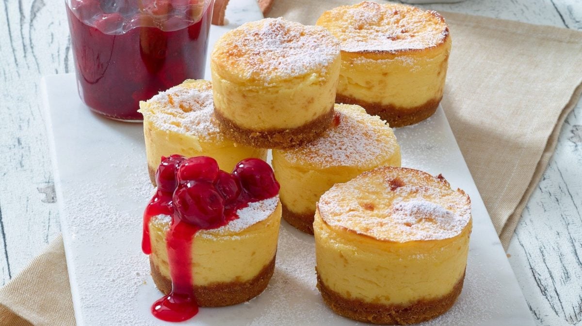 Unsere Cheesecake-Törtchen mit Kirch-Mousse stehen in Reih und Glied auf einer weißen Platte auf dem Tisch.