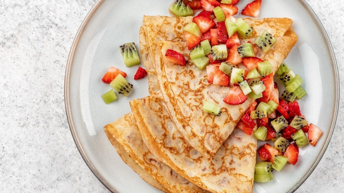 Unsere Crêpes mit Erdbeer-Kiwi-Salat liegen fein angerichtet auf einem Teller.