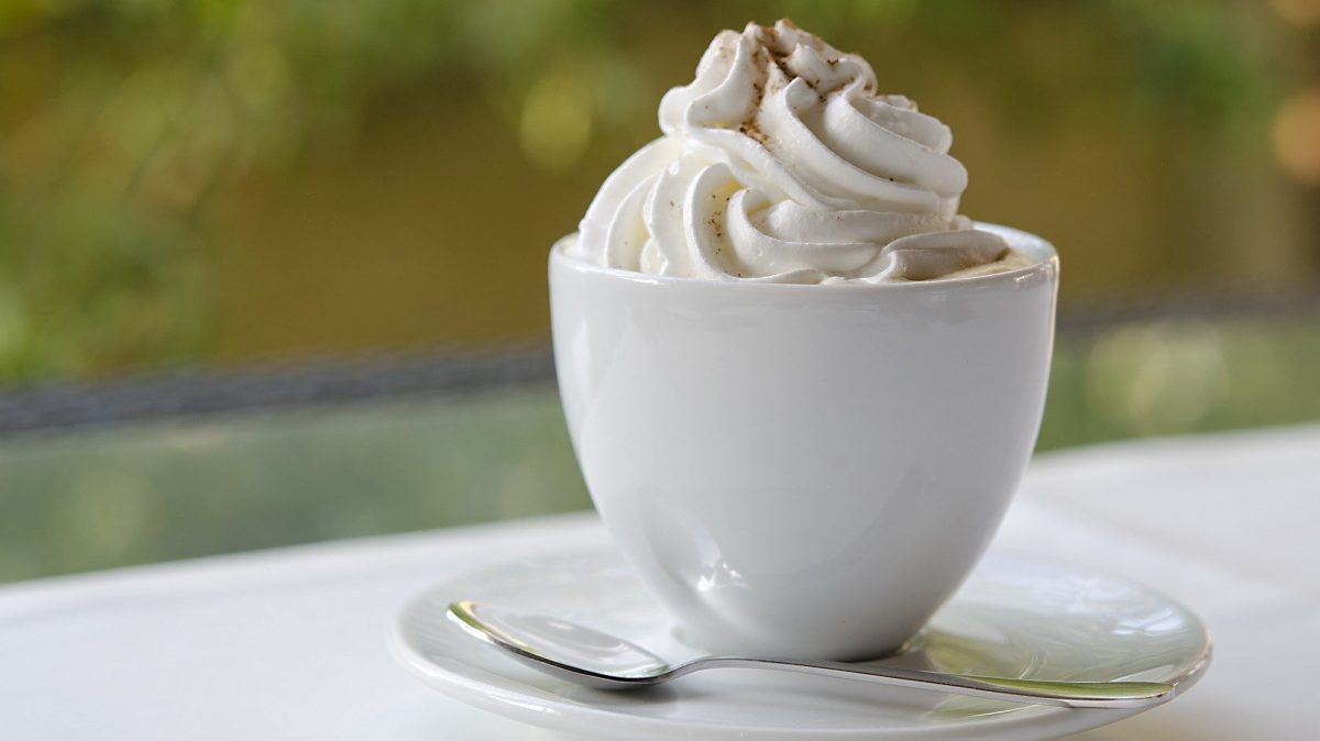 Auf einem Unterteller steht eine Tasse High-Tea wie im Londoner des 19. Jahrhunderts. Genieße diesen Earl Grey mit whipped Cream und träume von deinem Leben am englischen Königshof. Auf der Creme oben drauf ist etwas Kakaopulver.