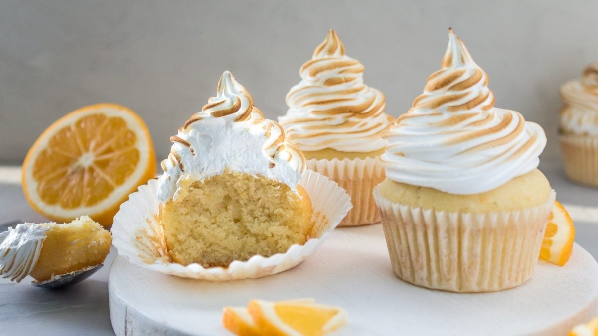 Auf einem Holzteller stehen drei Meringue Cupcakes. Sie sind mit Meringue Creme dekoriert. Die Creme ist karamellisiert.