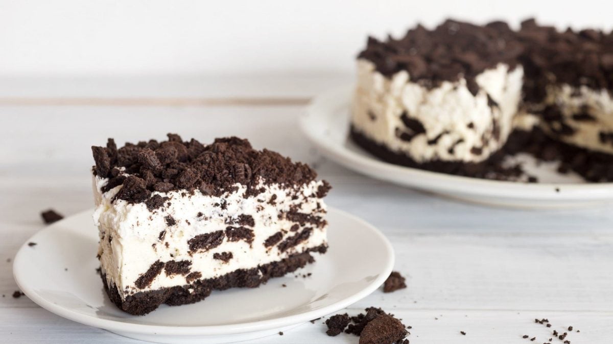 Auf einem Teller liegt ein Stück des Oreo Cheesecake. Er ist fluffig und cremig und oben mit Oreo-Keksen bedeckt.