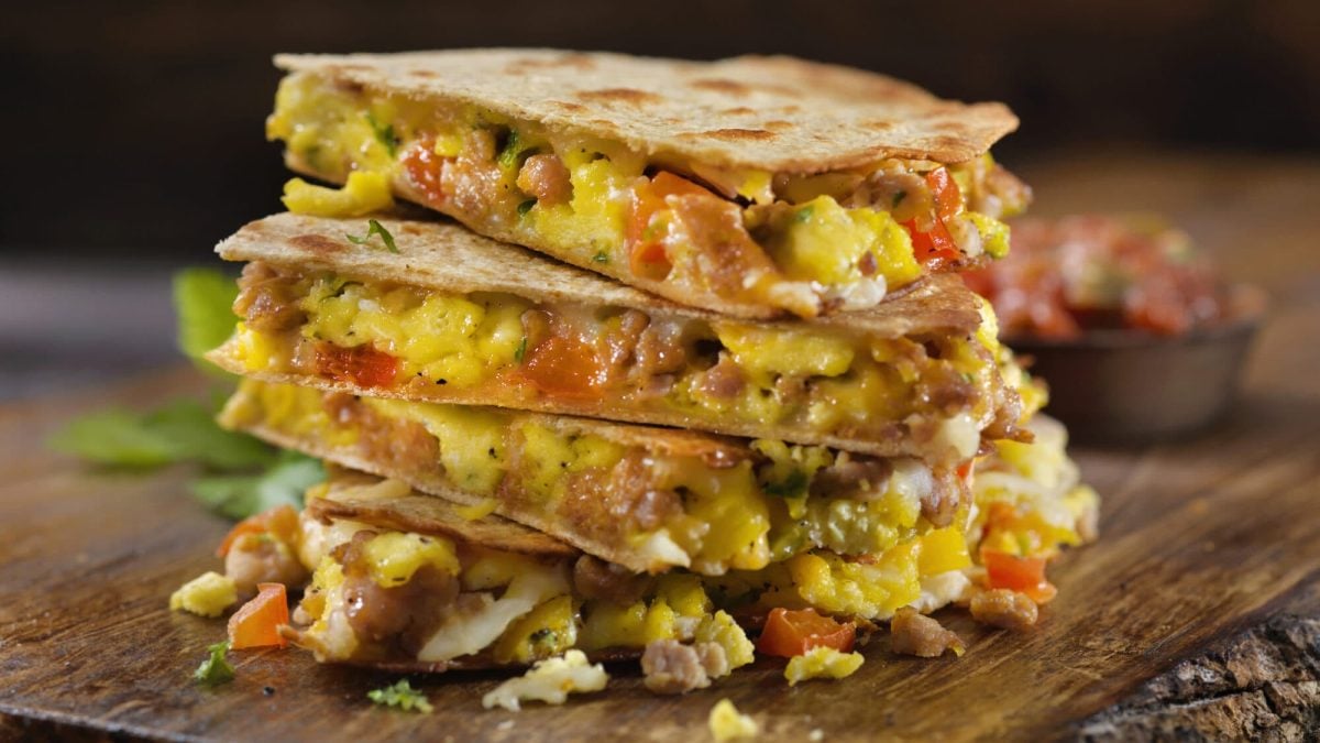 Unsere Frühstücks-Quesadillas liegen gestapelt auf einem Holzbrett.