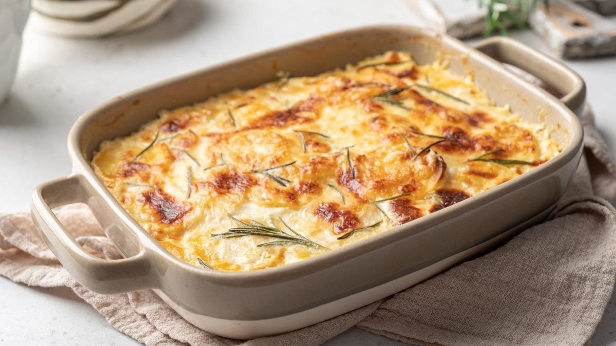 Weiße Auflaufform gefüllt mit Kartoffelgratin und Rosmarin.