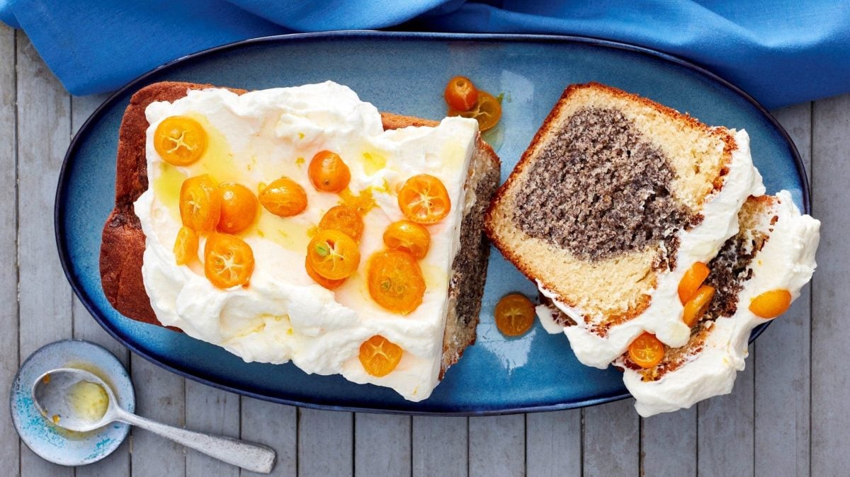 Unser Mohn-Joghurt-Kuchen liegt angeschnitten auf einer Kuchenplatte. Zwei Stücke sind abgeschnittenn.