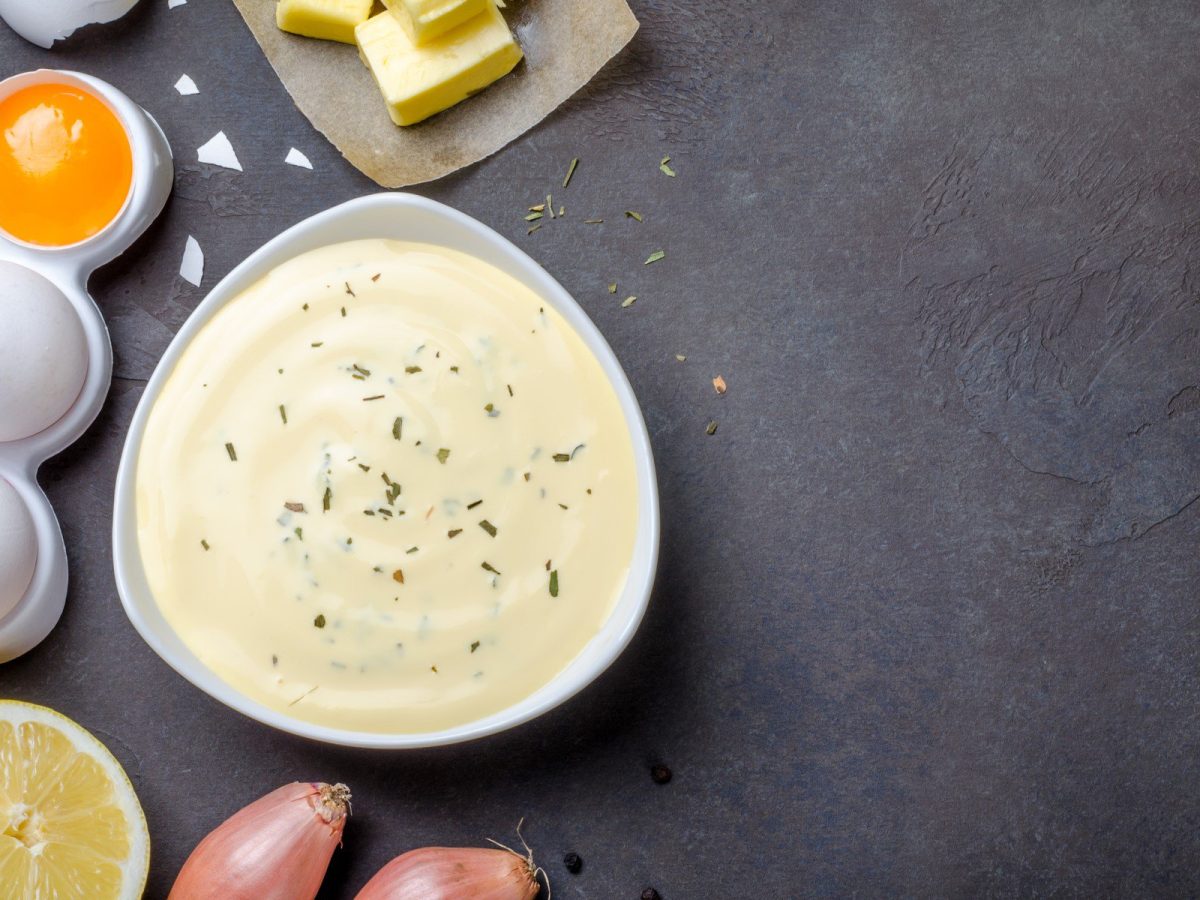 Sauce béarnaise mit den zugehörigen Zutaten auf dunklem Untergrund.