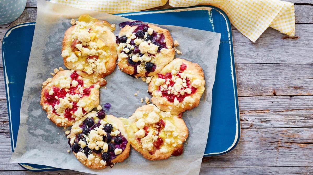 Unsere Streuseltaler-Tarte liegt angerichtet auf Butterbrotpapier auf einem blauen Holzbrett.