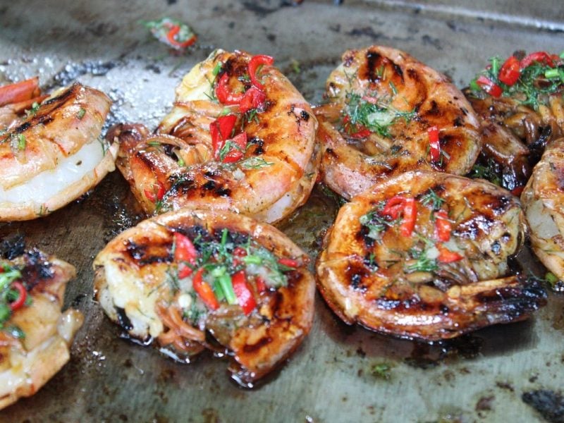 Garnelen auf dem Grill von oben fotografiert mit allerhand Kräutern und Gewürzen.