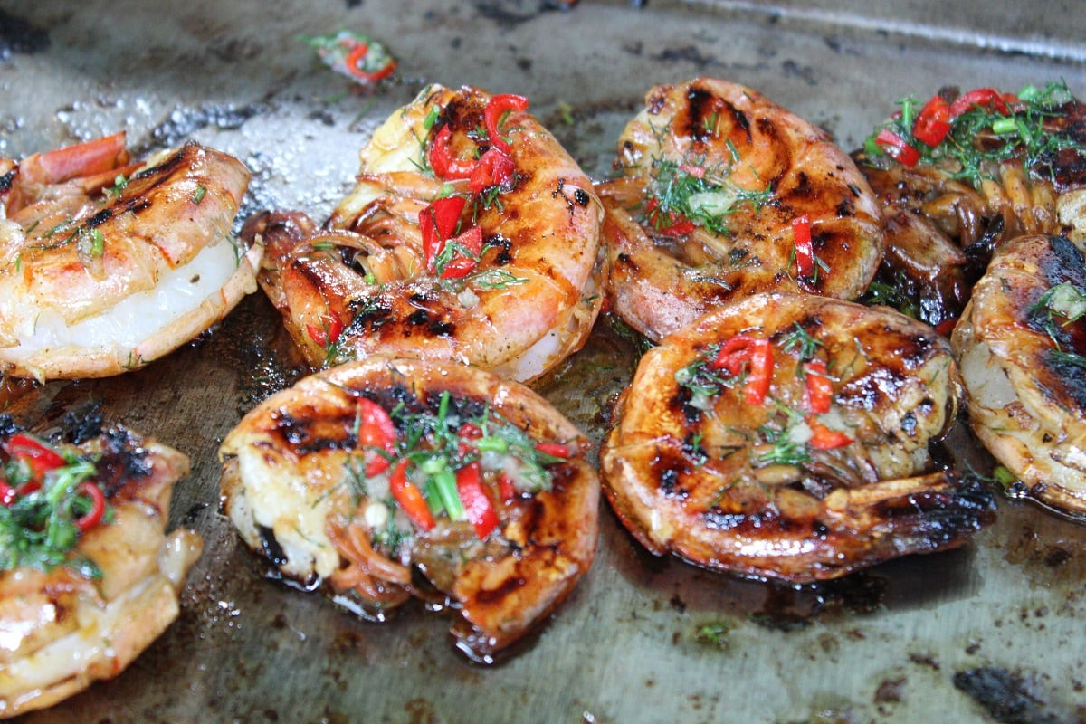 Garnelen auf dem Grill von oben fotografiert mit allerhand Kräutern und Gewürzen.