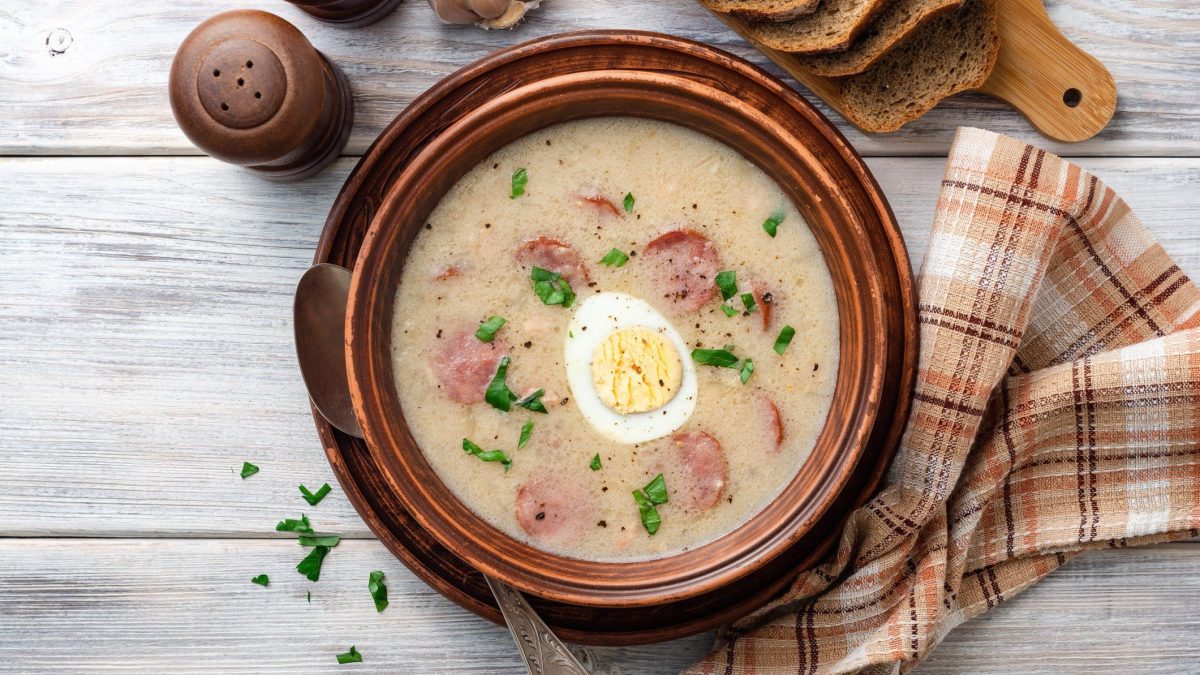 Polnische Ostersuppe Zurek in Tonschüssel auf hellem, hölzernen Untergrund.