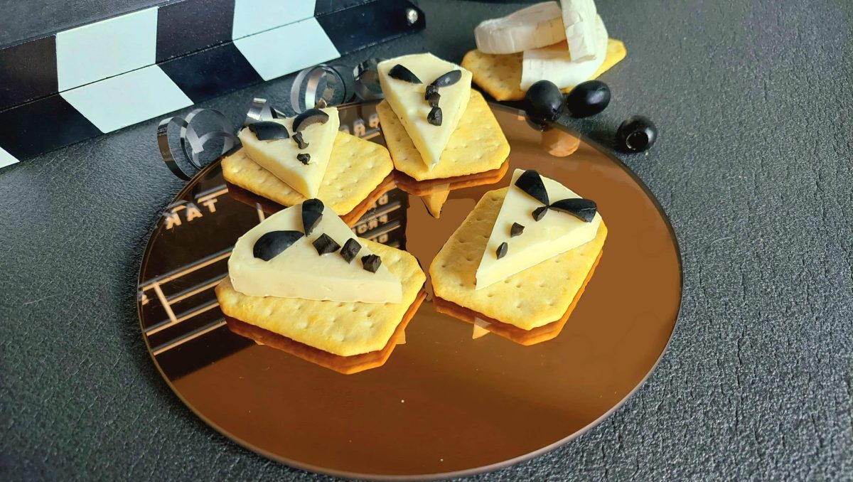 Draufsicht auf braunen verspiegelten teller mit herzhaften Keksen und Camembert mit Oliven in Anzugsform geschnitten.