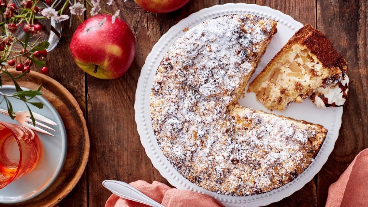 Apfel-Müslikuchen mit Puderzucker bestäubt auf einer Kuchenplatte auf einem dekorierten Holztisch
