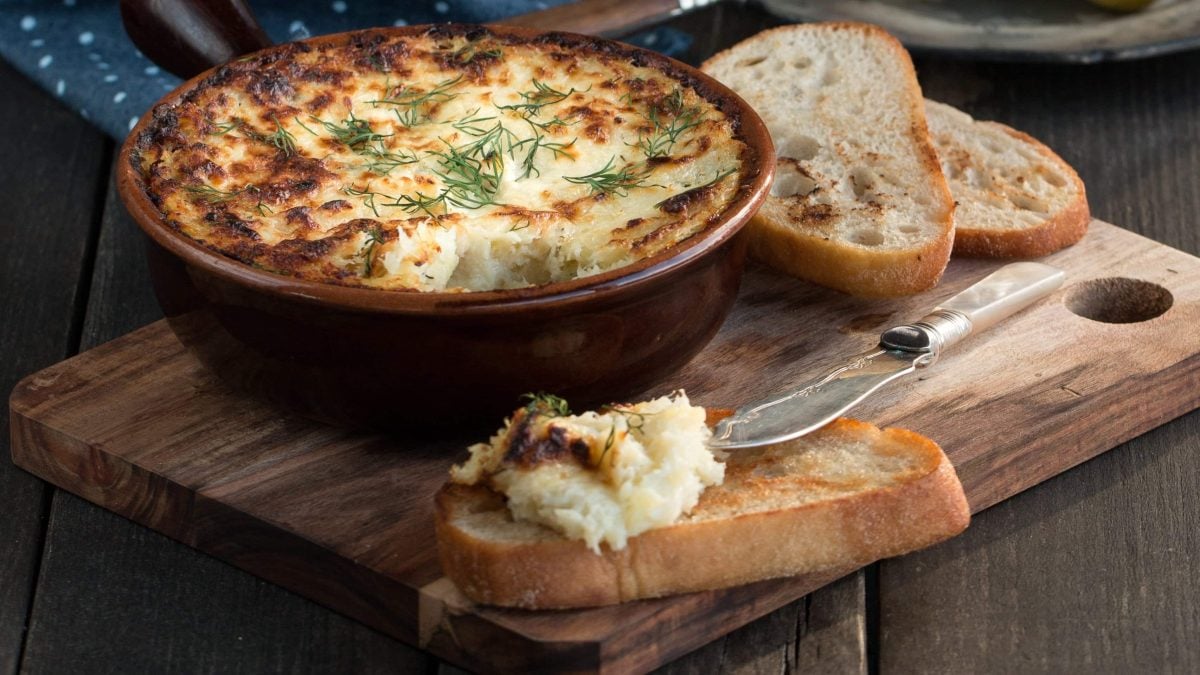 Auflaufform mit Brandade auf Holzbrett und Weißbrot mit dem Fischpüree.