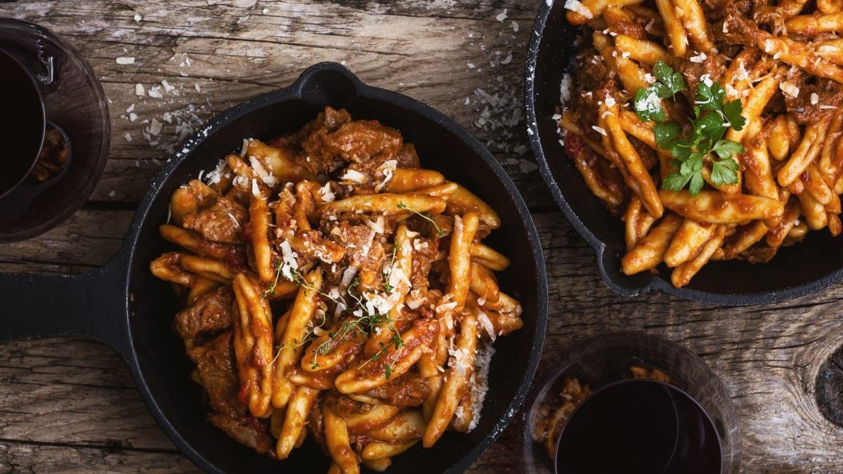 Casareccia Pasta mit Rinderragout in zwei gusseisernen Pfannen. Das Ganze auf einem hölzernen Untergrund.