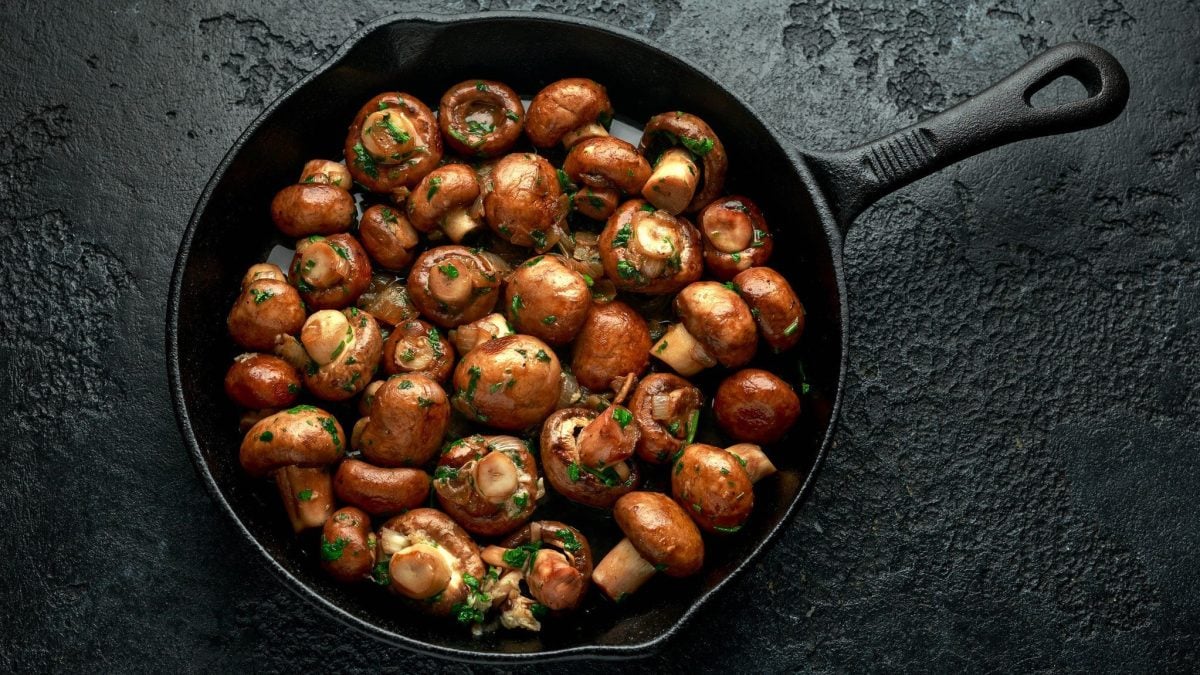 Eine Pfanne Champignons mit Sherrysauce auf dunklem Untergrund in der Draufsicht.