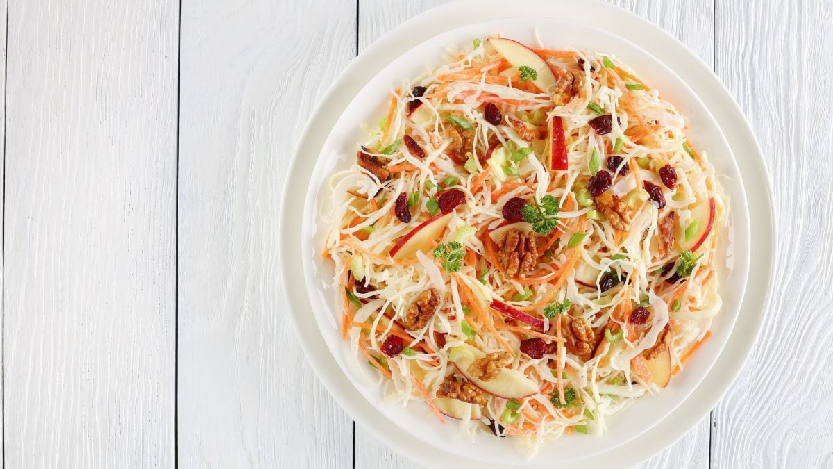 Ein Teller Coleslaw mit Äpfeln und Walnüssen auf hellem Holz in der Draufsicht.