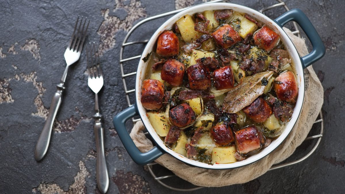 Saftiger Dublin Coddle mit Würstchen, Bacon und Kartoffeln in einer würzigen Biersauce, serviert in einem großen Topf auf steinernem Untergrund.